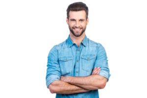 Confident young handsome man in jeans shirt keeping arms crossed and smiling while standing