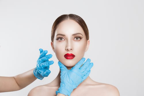 Closeup portrait doctor hands with gloves touching woman face chin lips chin want to change her form do plastic surgery-img-blog