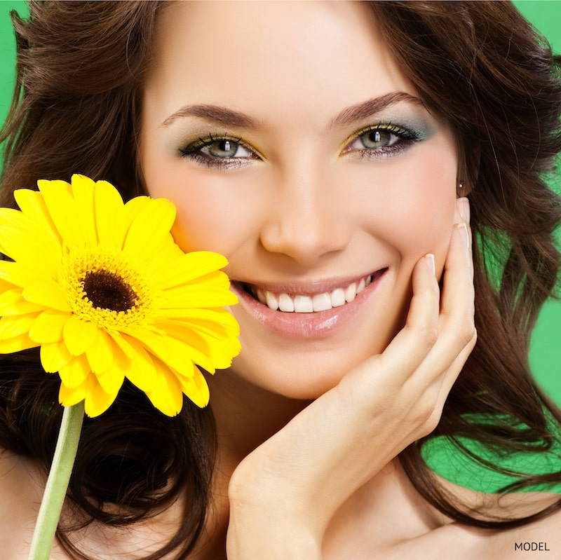 Young woman's face, holding a yellow flower against a green backdrop.