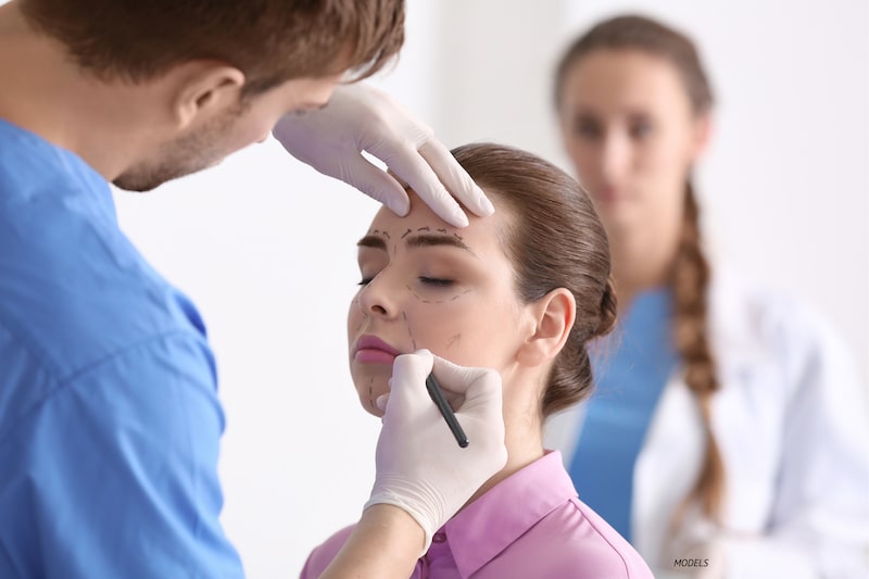 Woman getting lines drawn on face, as is for facial plastic surgery.