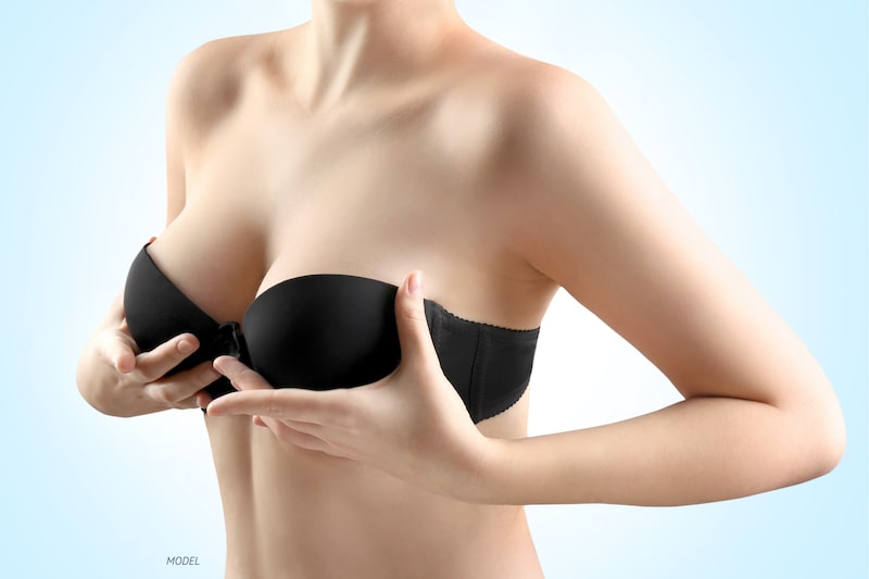 Woman holding up her breasts, wearing a black bra.