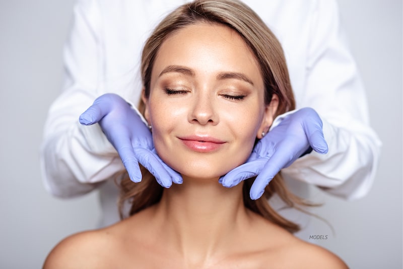 beautiful woman with closed eyes, smiling at the camera while a surgeon stands behind her