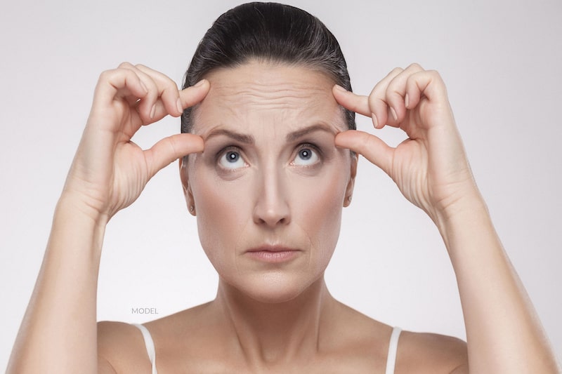 Middle-aged woman holding her hands to her forehead to examine the wrinkles in her upper face