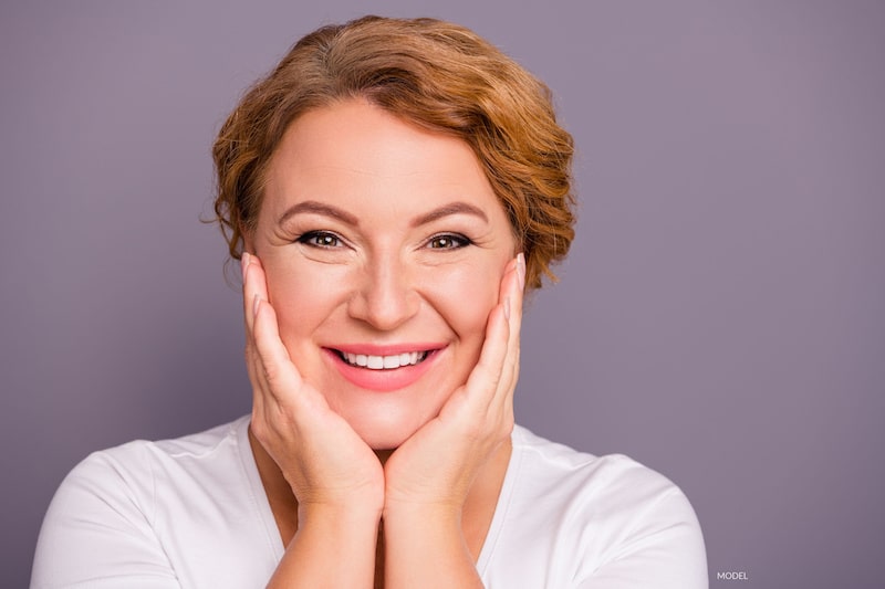 Middle-aged woman with smooth and beautiful skin and holding her hands on either side of her face.